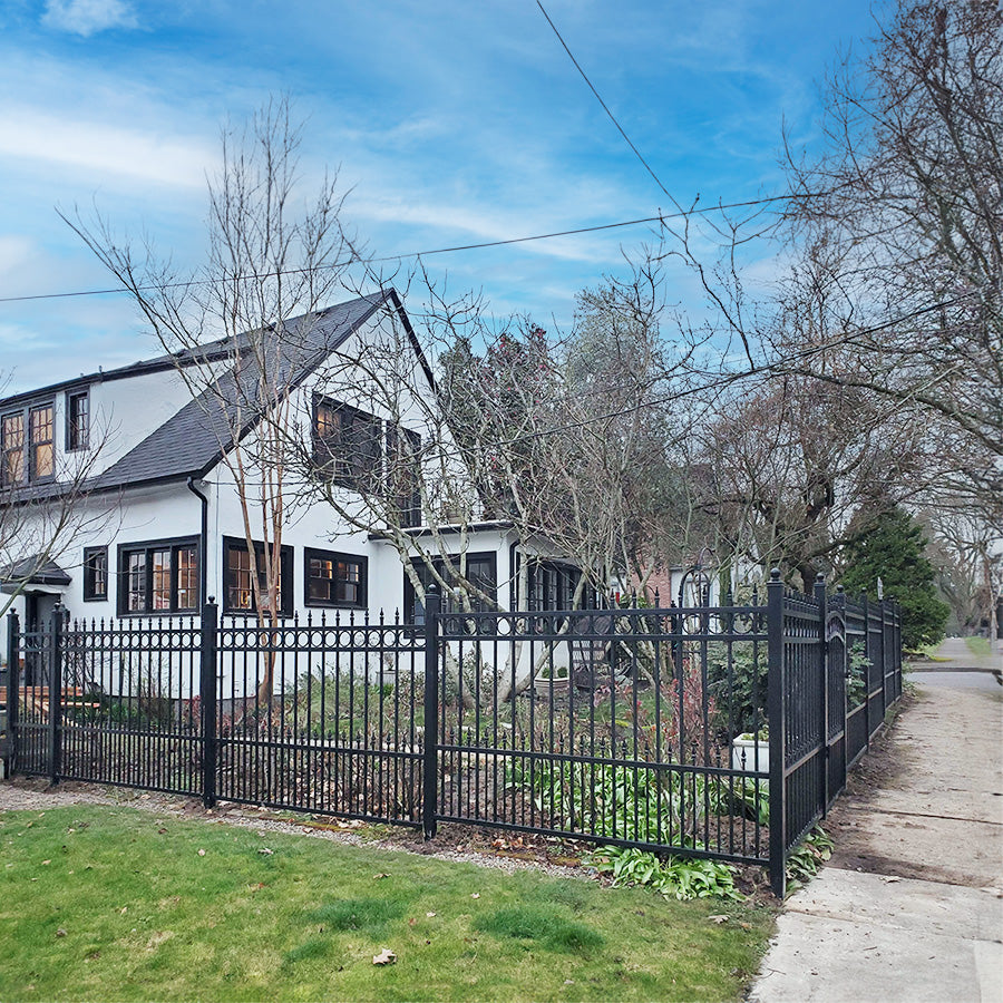 White brick house and garden surrounded by single black wrought iron fence with a row of circles trimming the top and spear point finials. Ball finials on fence posts.