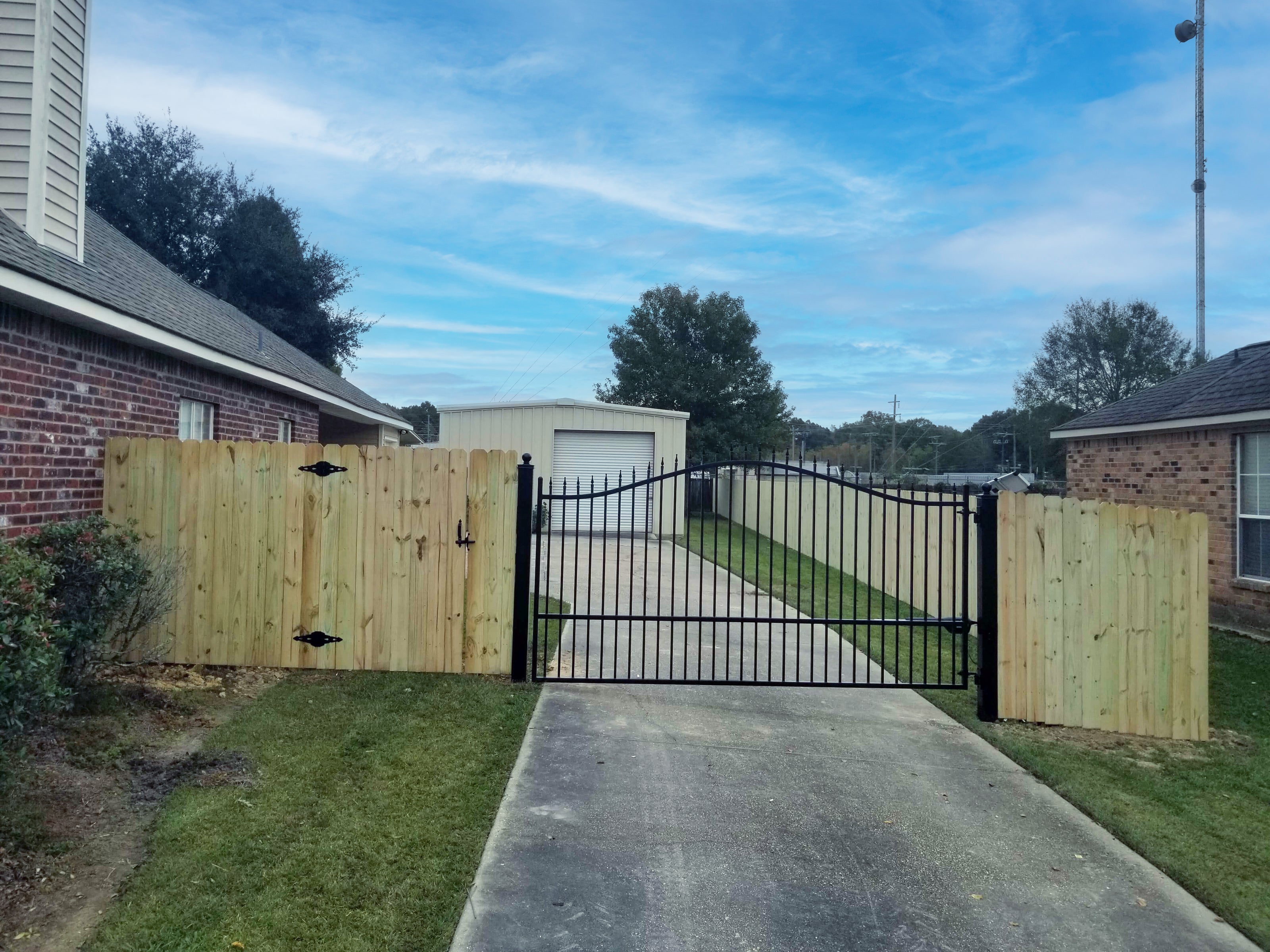 very simple black wrought iron single gate across a driveway mounted in wood fence around backyard of ranch home