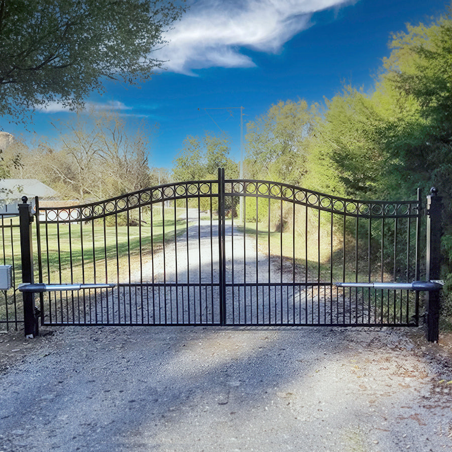 double arched black wrought iron gate with row of circles on top ball caps on both posts in front of long gravel driveway with blue sky with clouds