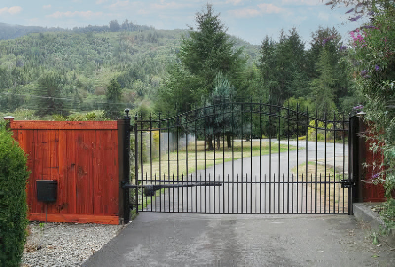 black wrought iron gate in front of winding drive lined with evergreens