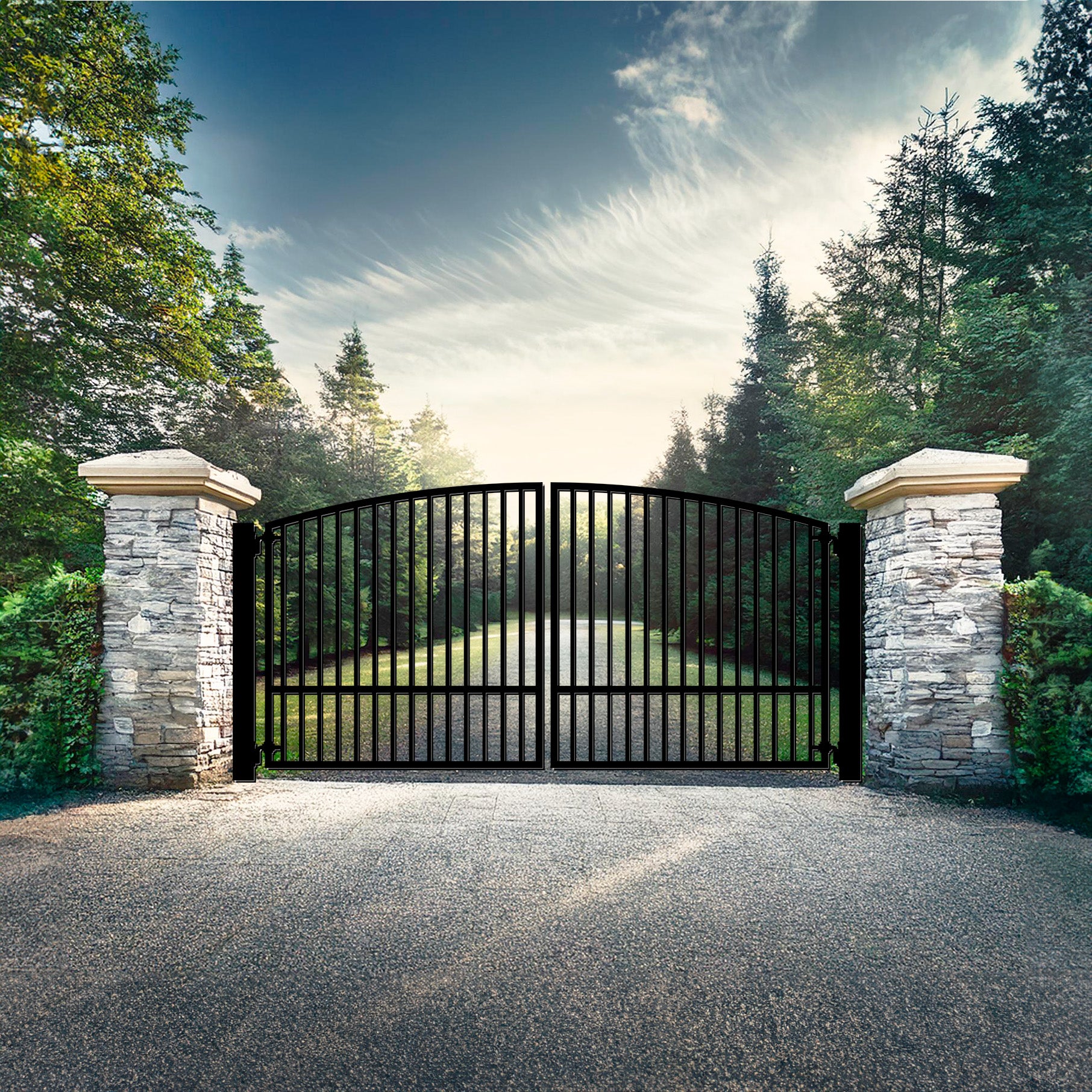 Black wrought iron gate with vertical bars and a curved top, flanked by stone pillars, leading to a tree-lined driveway.