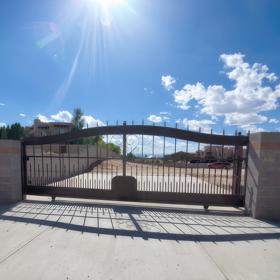 ornate arched black wrought iron  single slide gate at the end of a drive between concrete wall