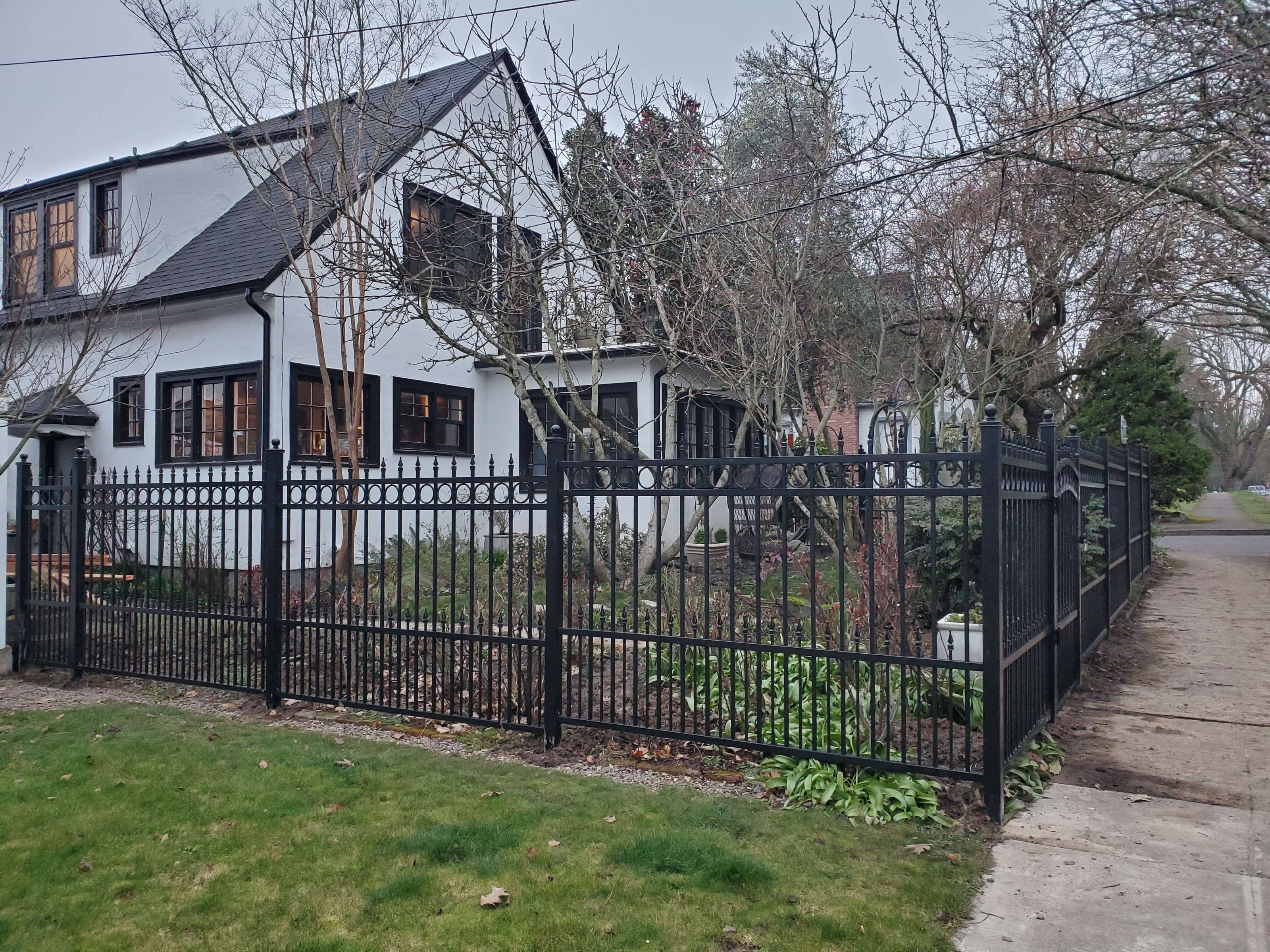 White brick house and garden surrounded by single black wrought iron fence with a row of circles trimming the top and spear point finials. Ball finials on fence posts.