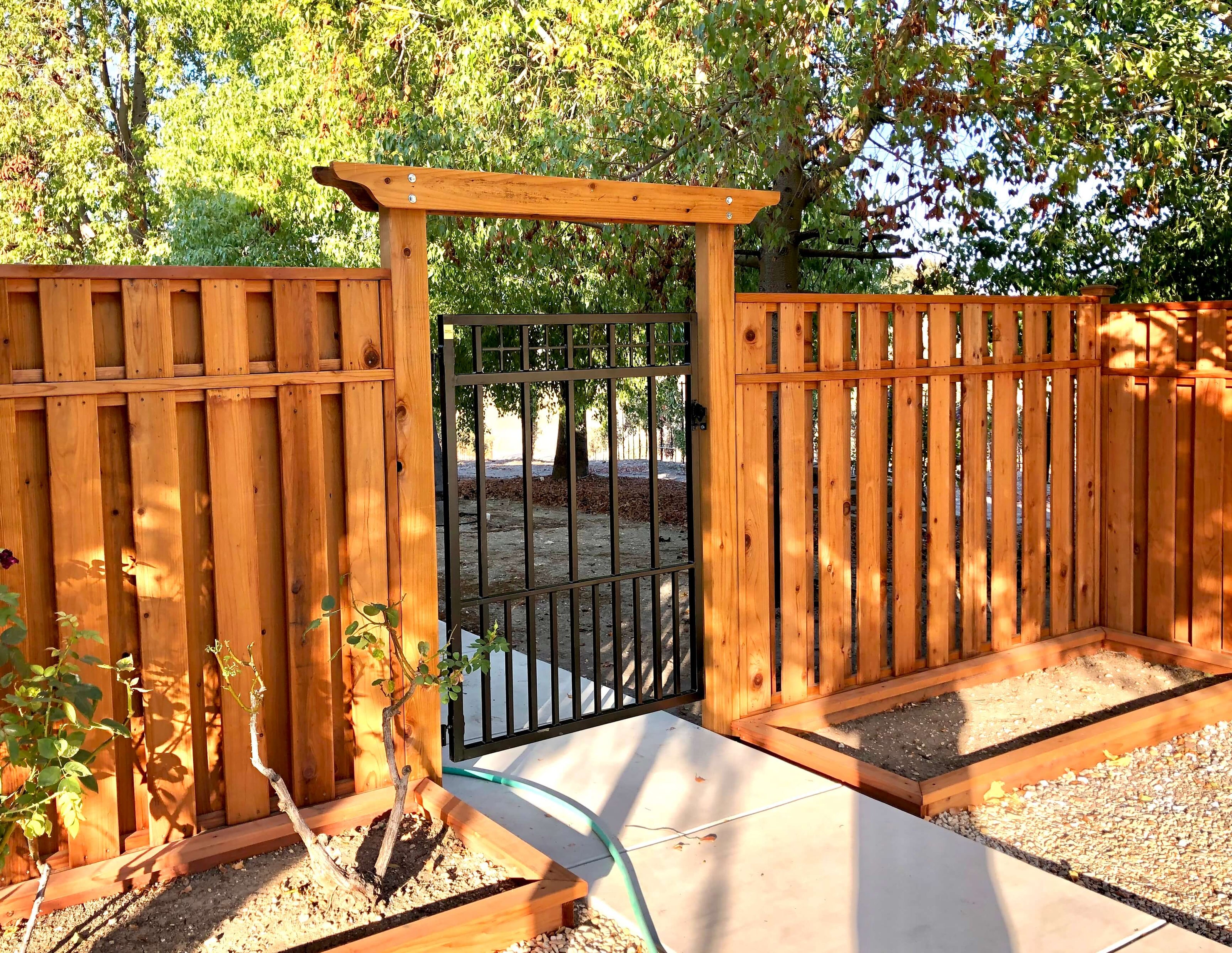 geometric wrought iron garden gate set in craftsman style wood fence stained redwood with arbor