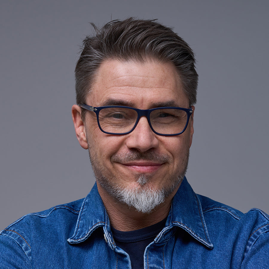 smiling male employee head shot in denim shirt with glasses