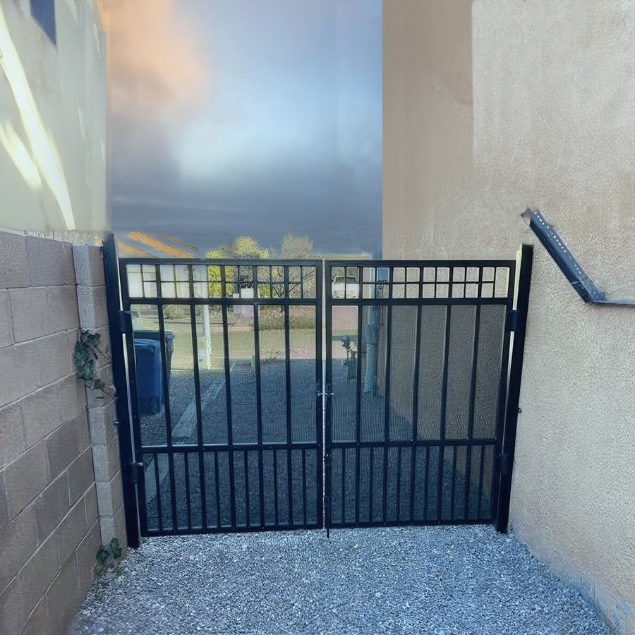 double pedestrian black metal gate attached to stucco wals of apartment building in gravel alley. Gate has ornamental grid pattern on top, vertical bars.