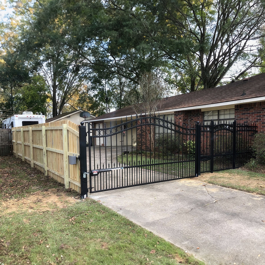 single black wrought iron gate that is arched with row of circles trimming the top and spear point finials.The gate is attached on one side to a brick ranch house. On the other to a wood fence.