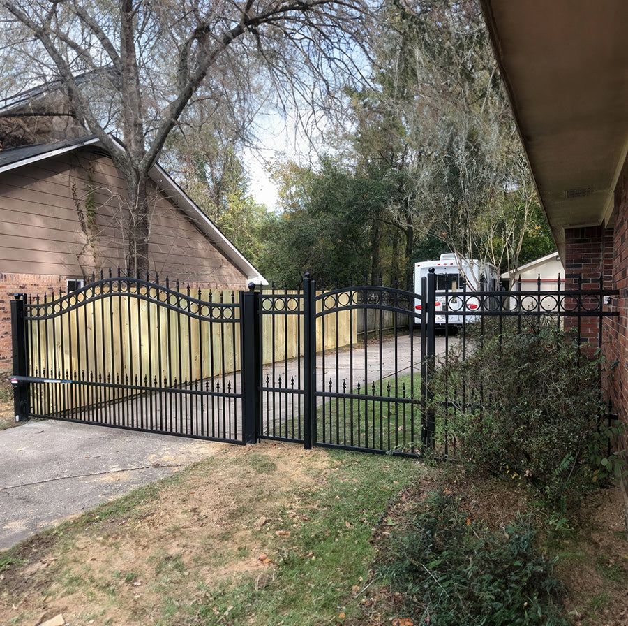 ten foot double black wrought iron gate attached to small matching fence and matching garden gate of brick ranch home on one side and pine fence on other side