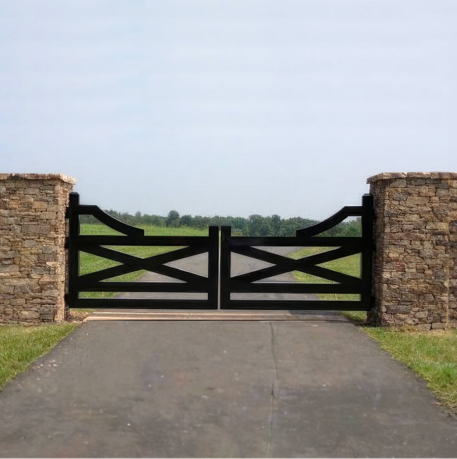 dark metal ranch style double gate with large heavy X motif hangs across long driveway between stacked stone columns