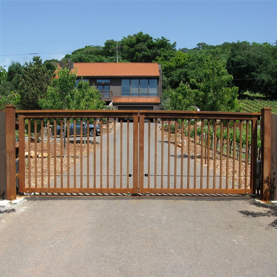 rust color simple gate with vertical bars installed on long drive to modern house with terra cotta roof surrounded by vineyard and blue sky