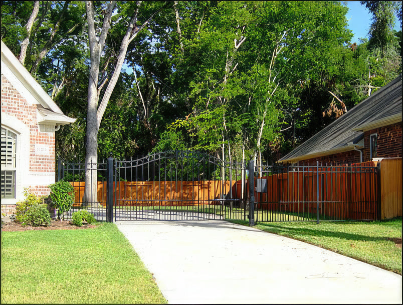 single black wrought iron gate that is arched with row of circles trimming the top and spear point finials with matching fence either side closing in side yard of brick home and manicured green lawn, trees and redwood fence around permiiter