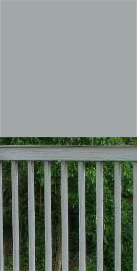 Close-up of a Pebble Beach color surface above a gray metal fence with vertical bars, set against a background of trees.