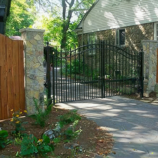ten foot double black wrought iron gate between stone square columns that is arched with row of circles trimming the top and spear point finials with matching fence either side closing in side yard of brick home on one side and redwood fence on other