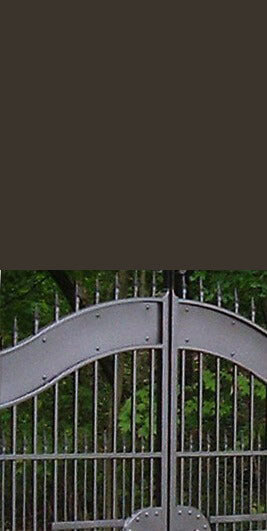 Close-up of a Architectural Bronze color surface above a bronze metal gate with a curved design and vertical bars.